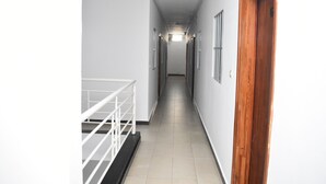 Um corredor estreito e bem iluminado, com paredes brancas e uma porta de madeira à direita.