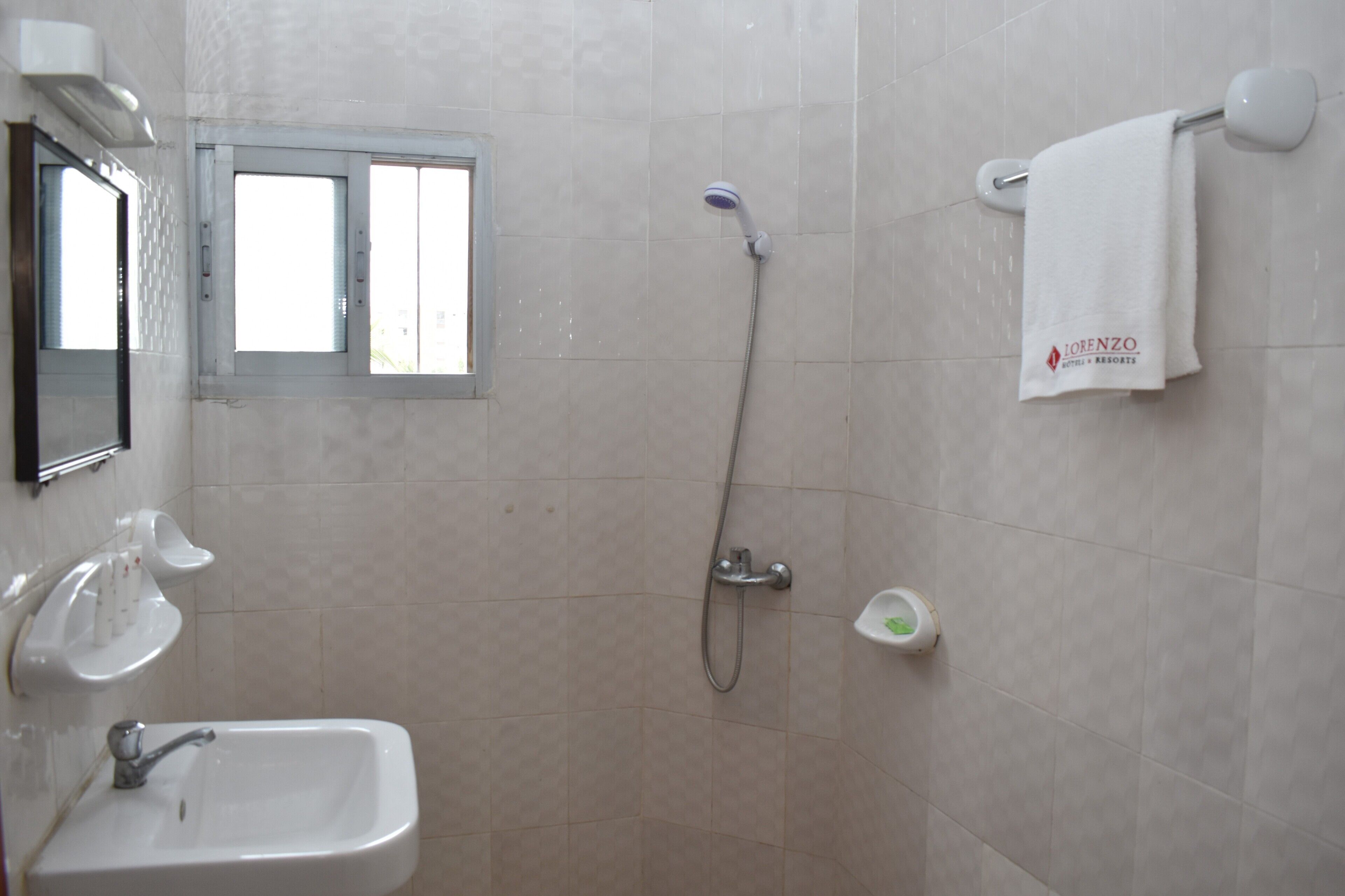 A bathroom with a sink, a handheld showerhead, a towel rack with a towel, and a window.