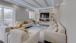 A modern living room with a sofa set, a glass coffee table, and a flat-screen TV mounted on the wall. - Exquisite Custom-Built 5 BDRM Multi-Level Estate (Mississauga)