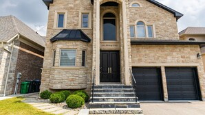 A two-story stone house with a black front door, a garage, and a small front yard with bushes. - Exquisite Custom-Built 5 BDRM Multi-Level Estate (Mississauga)