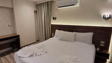 Ein Hotelzimmer mit einem großen Bett, zwei Kissen, einer Klimaanlage, einem Nachttisch mit Telefon und einer Wandleuchte.