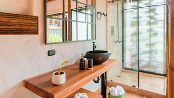 A modern bathroom with a wooden vanity, a large mirror, a black sink, and a glass shower enclosure.