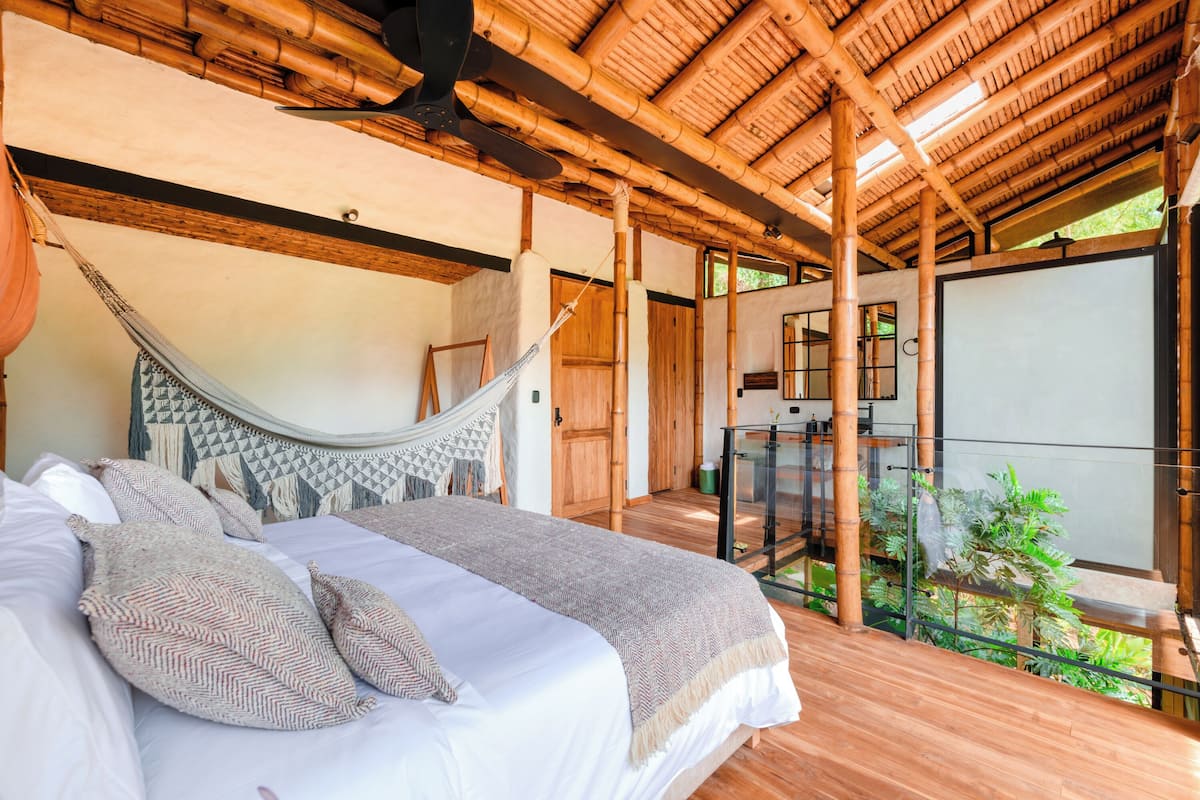 Une chambre spacieuse avec un grand lit, un hamac et un balcon vitré agrémenté de plantes.