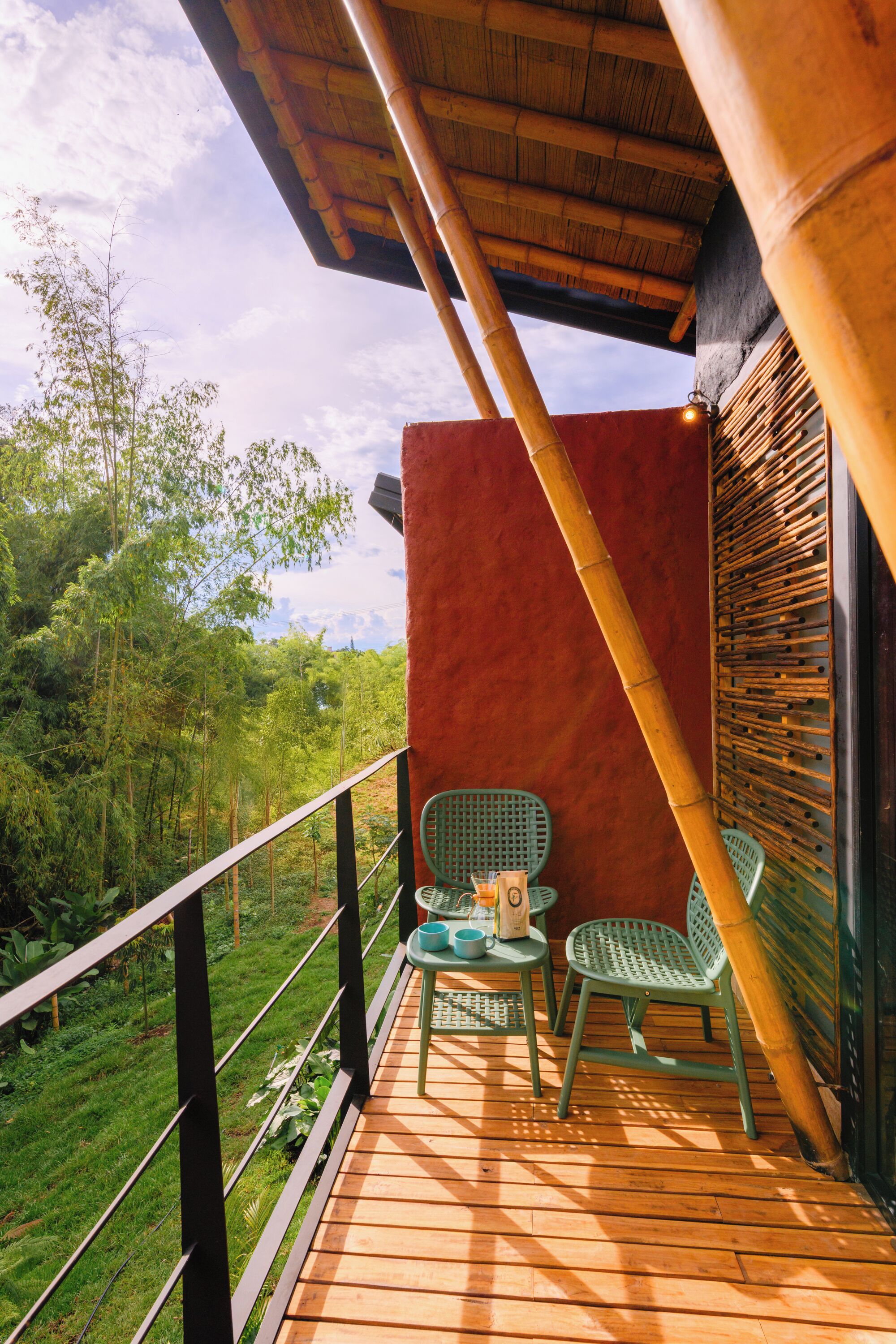 A wooden deck with two green chairs and a table, overlooking a lush green landscape.