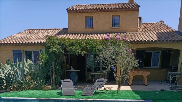 A swimming pool with a stone edge, surrounded by artificial grass and a patio area with chairs and a table. - Air-conditioned villa with large swimming pool (Le Pouget)