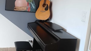 A piano with a guitar leaning against it, a framed painting on the wall, and a black chair in front of the piano. - Air-conditioned villa with large swimming pool (Le Pouget)