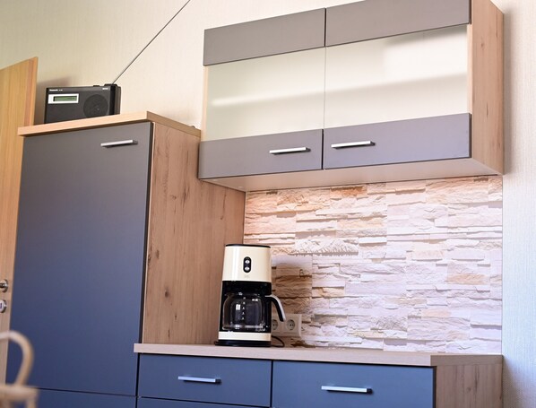 A kitchen with a coffee maker, a radio, and a stone-textured backsplash.