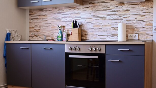 Eine Küche mit Steinrückwand, einem eingebauten Ofen und einem Holzbesteckhalter.