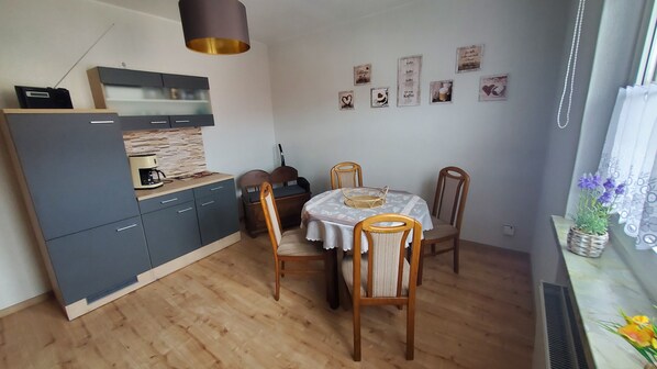 A compact kitchen with a coffee maker, a dining table with chairs, and a small window with a plant.