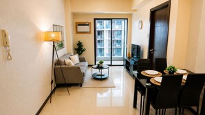 A modern living room with a sofa, coffee table, dining table with chairs, and a TV. - Manila Bay View - 1BR with balcony (Pasay)