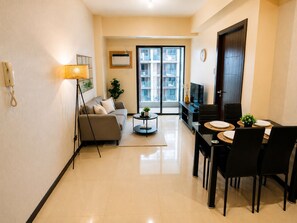 A modern living room with a sofa, coffee table, dining table with chairs, and a TV. - Manila Bay View - 1BR with balcony (Pasay)