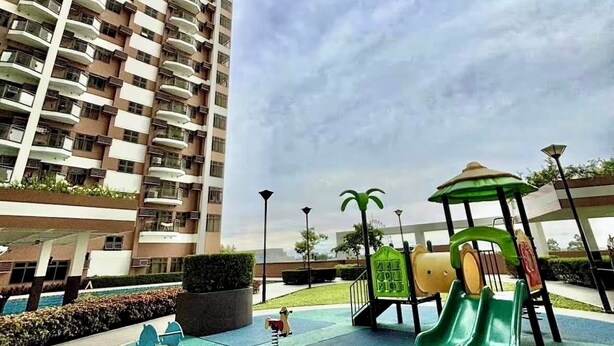 A playground with slides and swings, surrounded by a tall residential building. - Manila Bay View - 1BR with balcony (Pasay)