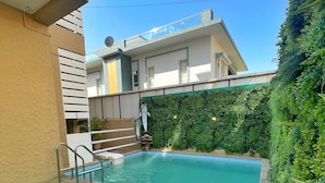 Una piscina con cubierta verde, rodeada por un seto y un edificio con balcón.