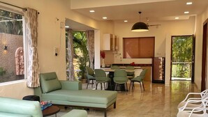 Amplia sala de estar con sofá, sillas, una mesa de comedor y una cocina al fondo.
