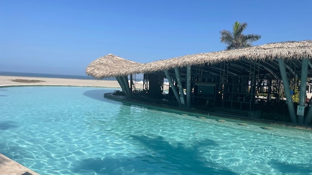 A poolside bar with a thatched roof, overlooking a beach.