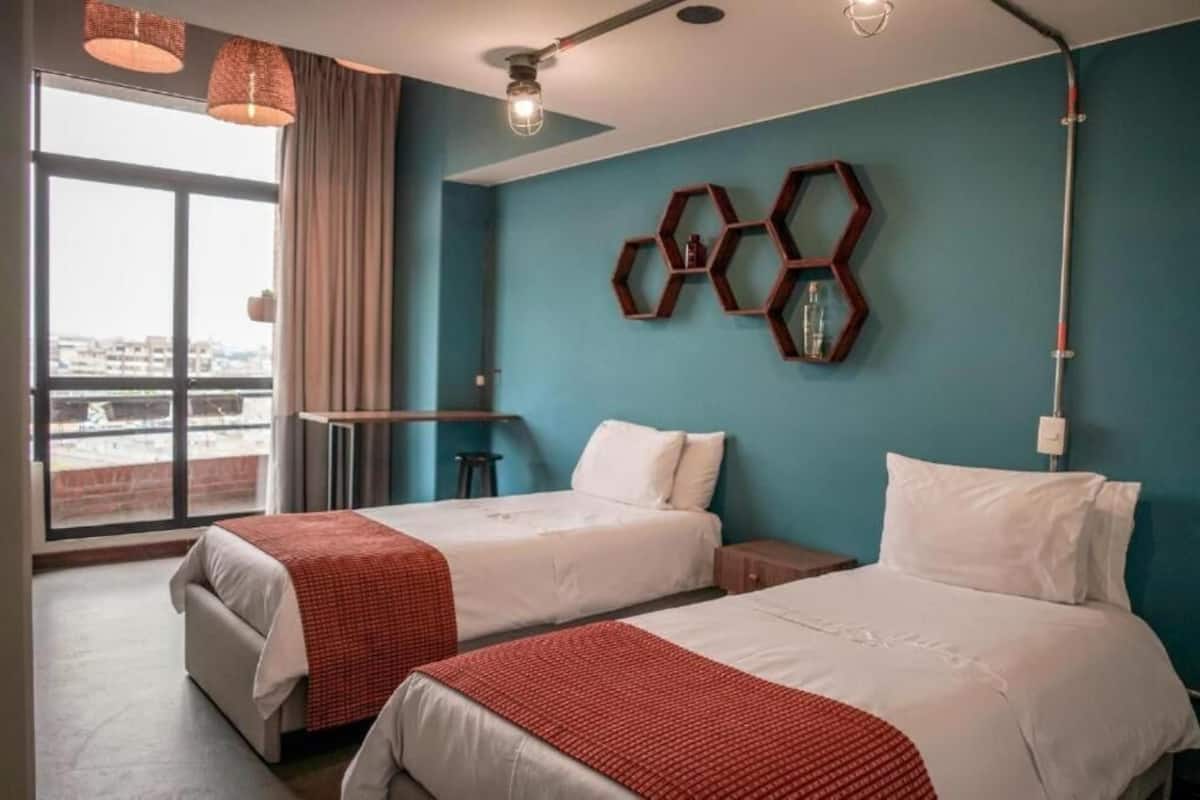 A hotel room with two beds, a desk, a large window with a view, and hexagonal wall decor.