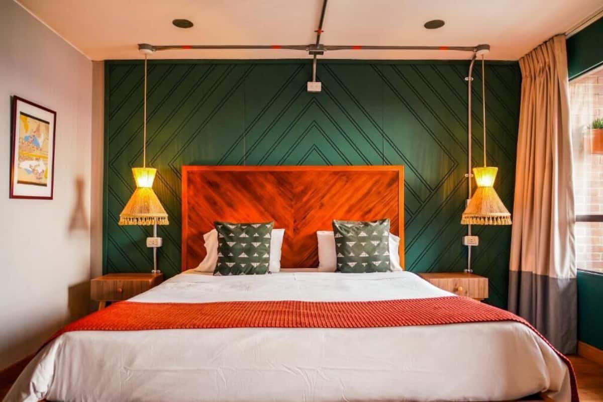 A hotel room with a large bed, two bedside lamps, a wooden headboard, and a green patterned wall.