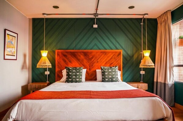 Une chambre d’hôtel avec un grand lit, deux lampes de chevet, une tête de lit en bois et un mur orné d’un motif vert.