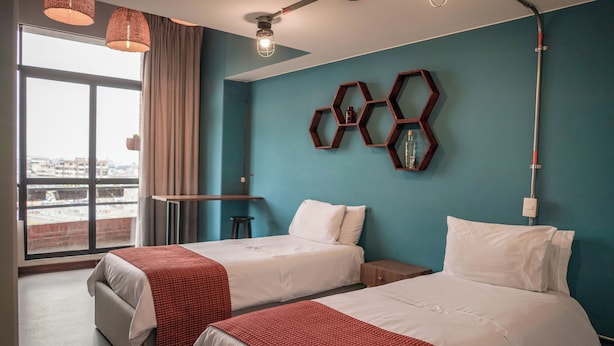 A hotel room with two beds, a large window with a view, a desk, and a wall-mounted hexagonal shelf. - Hotel San Felipe 74 (Bogota)