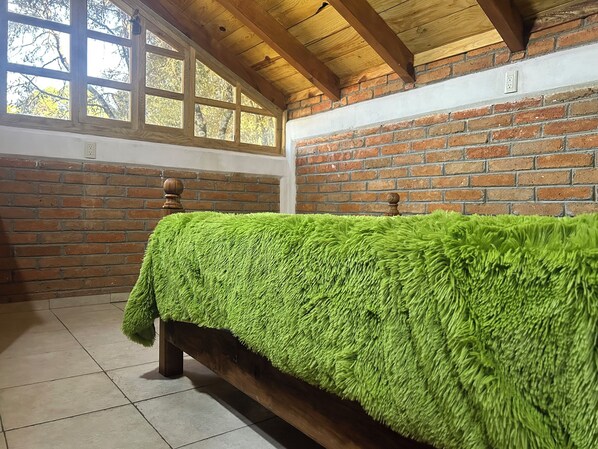 Una habitación con una cama de madera, una pared de ladrillo y una ventana.