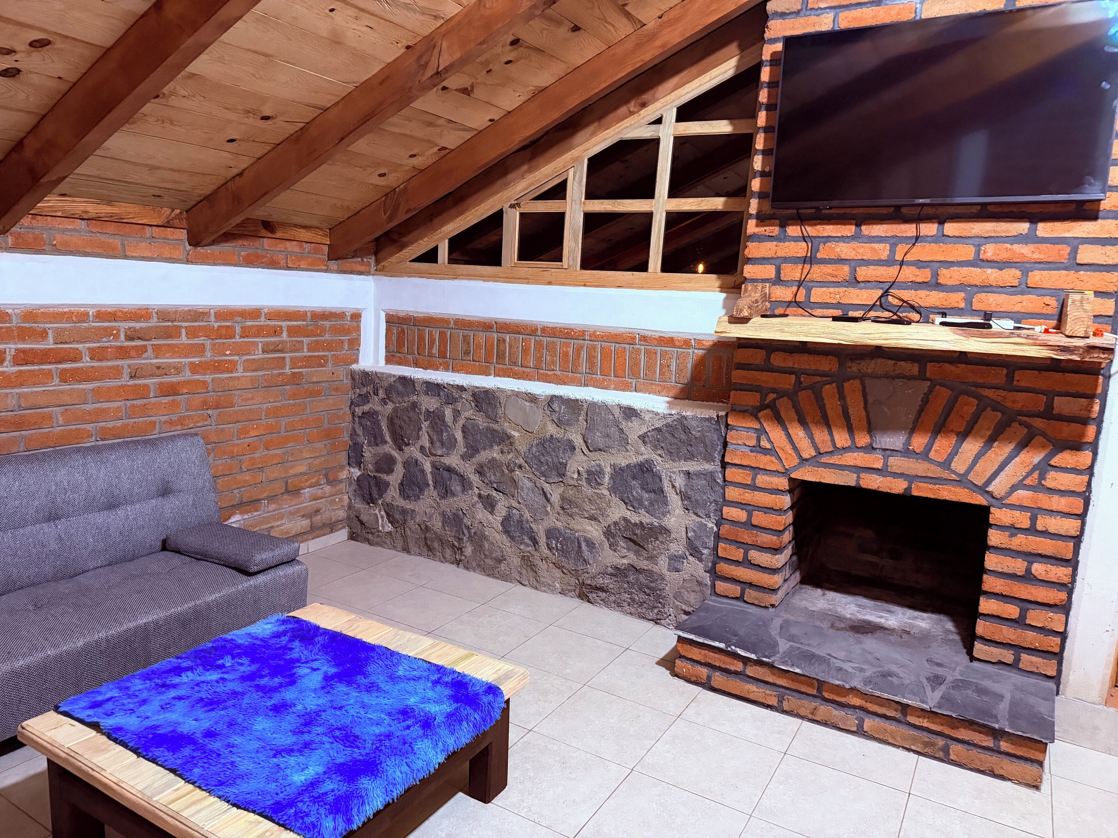 Un patio al aire libre con una chimenea de ladrillo, un televisor montado encima y un sofá gris.
