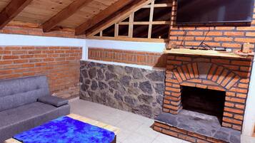 Un patio al aire libre con una chimenea de ladrillo, un televisor montado encima y un sofá gris.