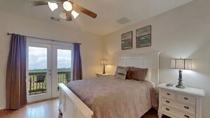 A bedroom with a bed, bedside tables, a ceiling fan, and a view through a sliding door. - Sandy Hook by Ryson Vacation Rentals (Galveston)