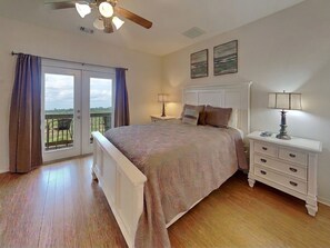 A bedroom with a bed, bedside tables, a ceiling fan, and a view through a sliding door.