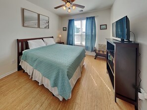 A bedroom with a bed, a desk, a television, and a ceiling fan. - Sandy Hook by Ryson Vacation Rentals (Galveston)