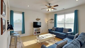 A living room with a sofa, a coffee table, a TV, and a ceiling fan. - Sandy Hook by Ryson Vacation Rentals (Galveston)