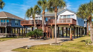 A beachfront property with multiple-story houses, wooden balconies, and palm trees. - Casa de Reyes by Ryson Vacation Rentals (Galveston)