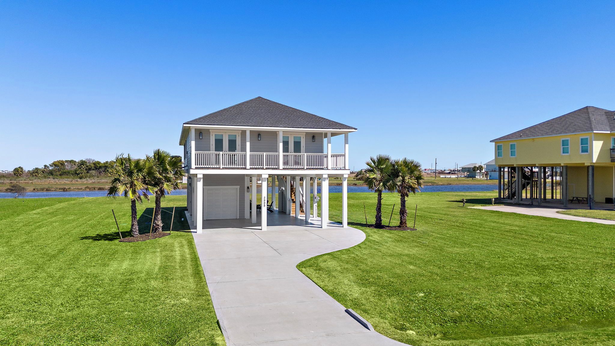 A two-story house with a balcony and a covered porch, surrounded by well-maintained grass and palm trees.