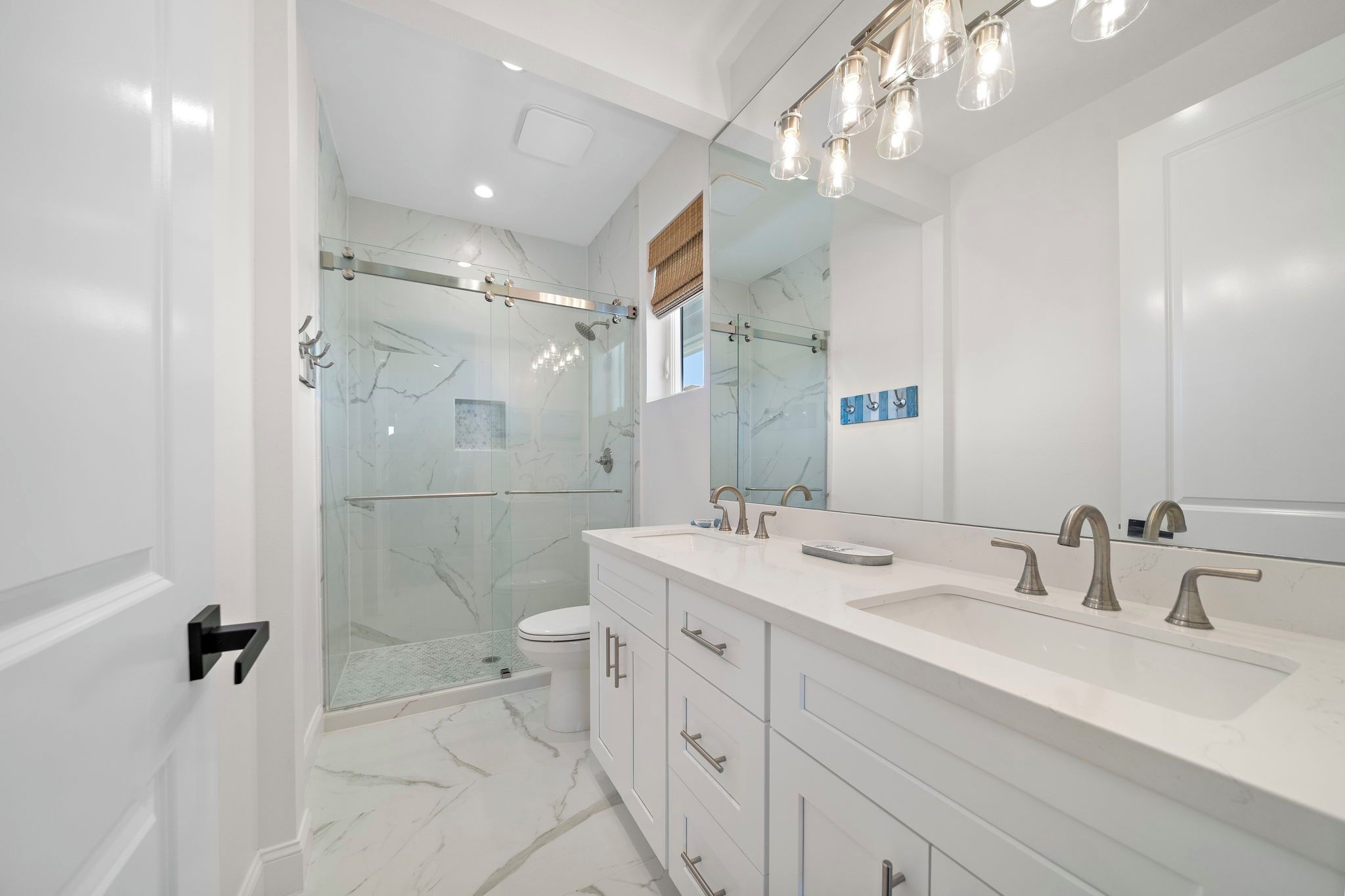 Un baño moderno con ducha de vidrio, un espejo grande y un tocador blanco con varios lavamanos.