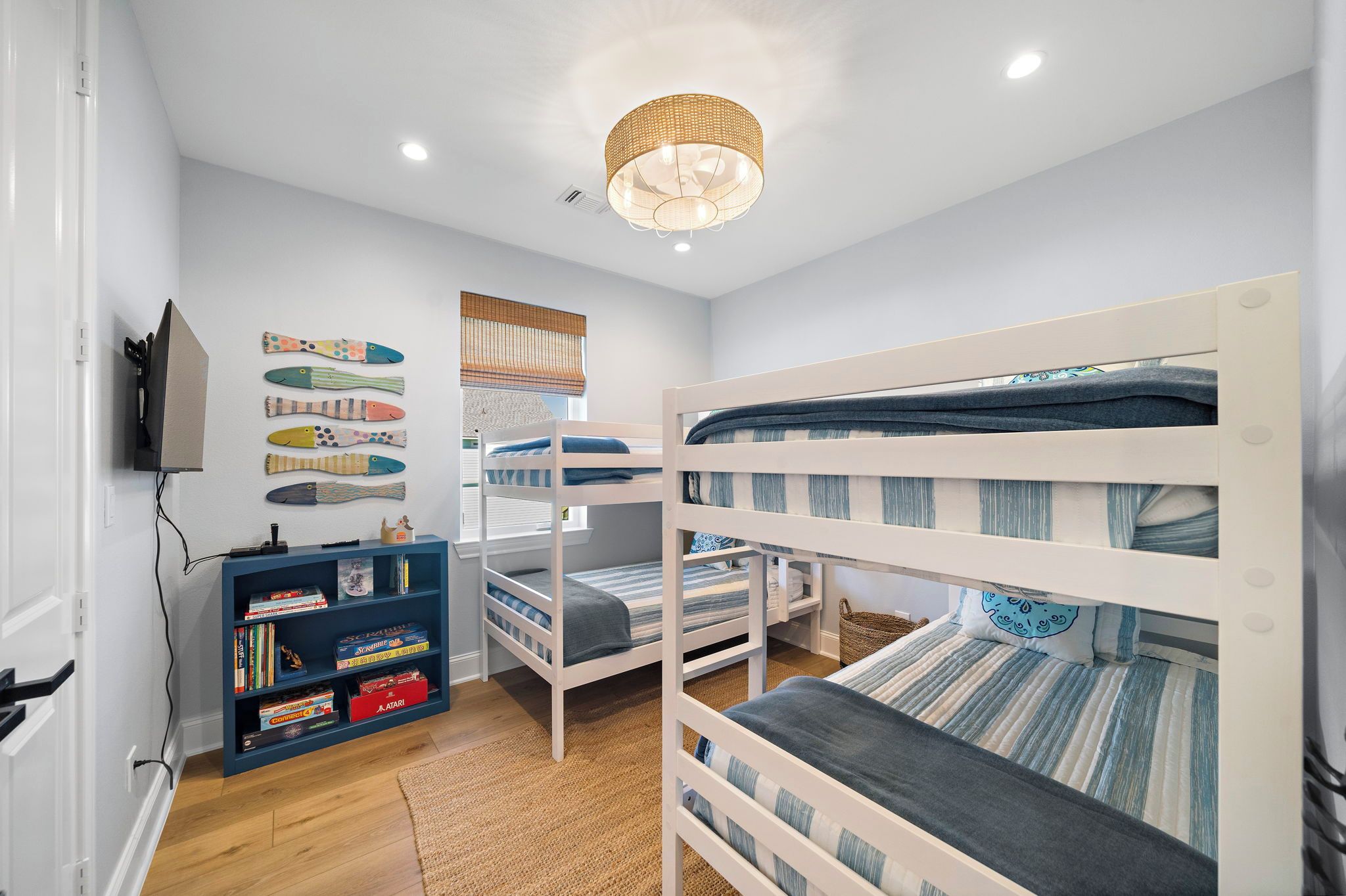 A bunk bed room with a bookshelf, a woven light fixture, and a window with blinds.