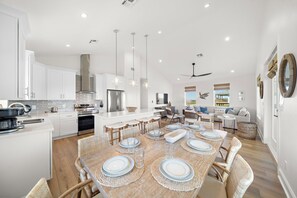 A modern kitchen with white cabinetry, stainless steel appliances, and a dining area with a wooden table set for six. - Pelican Perch by Ryson Vacation Rentals (Galveston)