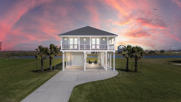 A two-story house with a balcony, a covered patio, and a view of a body of water during sunset. - Pelican Perch by Ryson Vacation Rentals (Galveston)