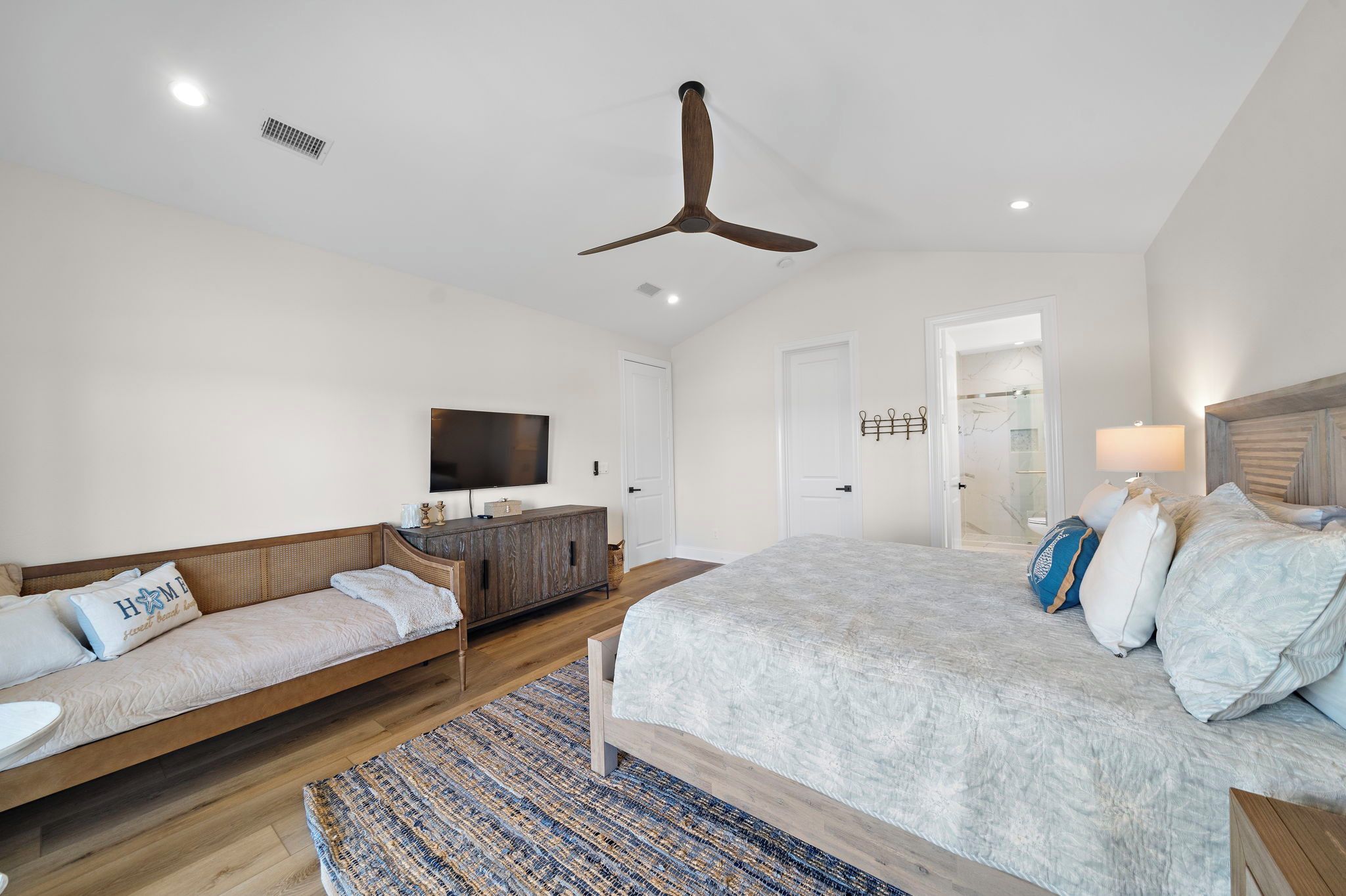 A bedroom with a bed, a sofa, a TV, and a ceiling fan.