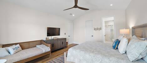 Quarto com cama, sofá, televisão e ventilador de teto.