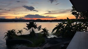 Vista de un lago al atardecer, con palmeras y un puente de piedra.
