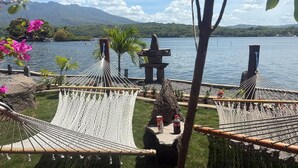 Una hamaca frente a un lago, con vistas a montañas y un pequeño templo al fondo.
