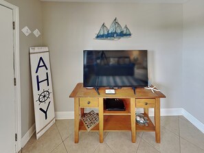 A wooden TV stand with a flat-screen TV, a small shelf, and a decorative sailboat on the wall.