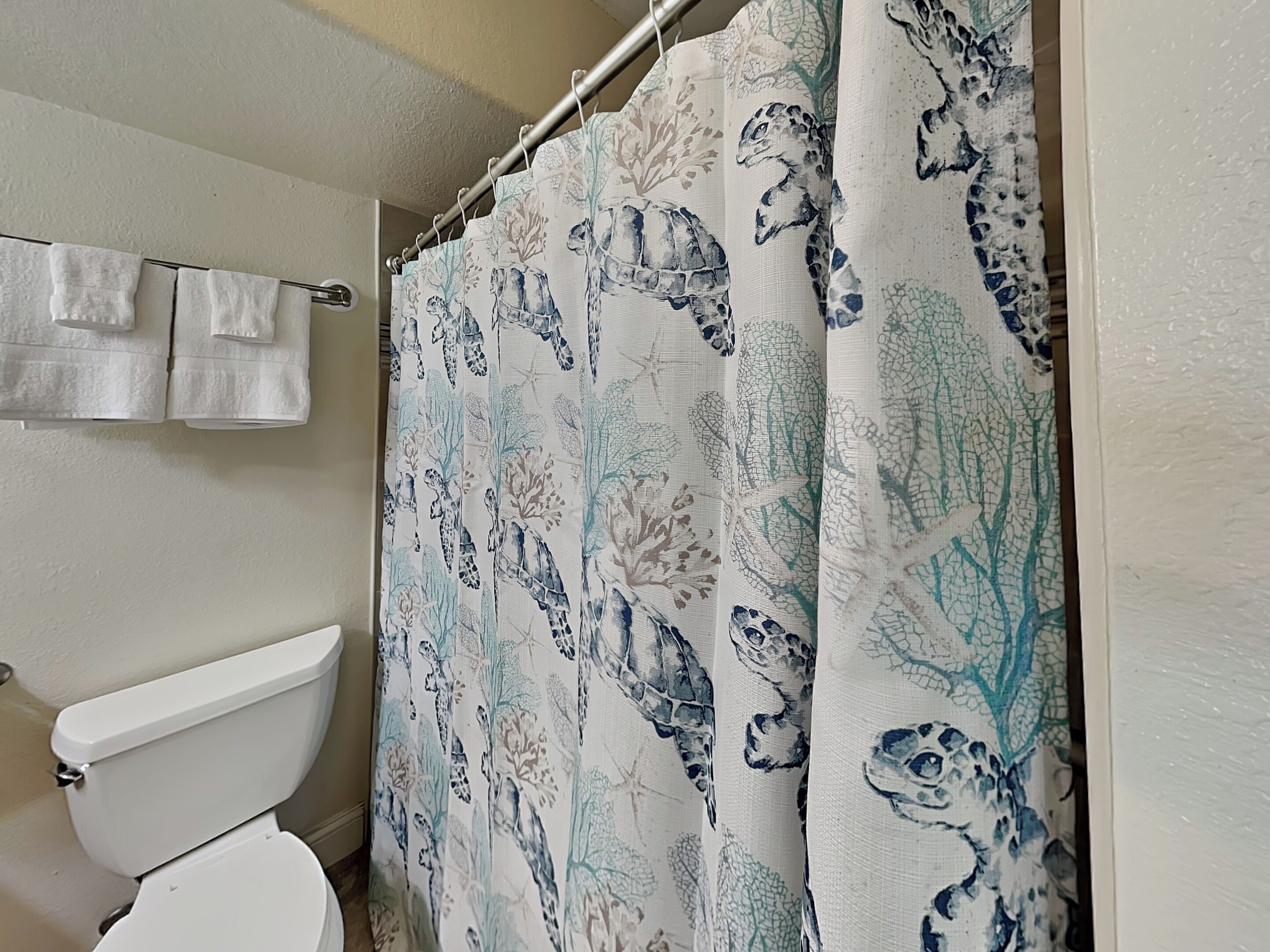 A bathroom with a toilet, a shower curtain with a nature-themed pattern, and a towel rack with two white towels.