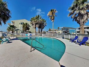 A swimming pool with a curved edge, surrounded by a white fence and blue chairs. - Beach...Please by Miss Kitty’s (Rockport)
