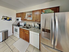 A modern kitchen with wooden cabinets, stainless steel appliances, and a 'Big Tuna' sign on the wall. - Something's Fishsea by Miss Kitty’s (Rockport)