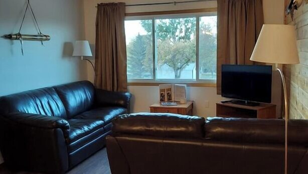 A living room with a black leather sofa, a television on a wooden stand, and a window with curtains.