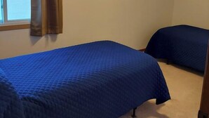 A bedroom with two beds, a window with brown curtains, and a beige carpet.