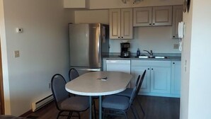 A compact kitchen with white cabinets, a stainless steel refrigerator, a dishwasher, and a small dining table with two chairs.