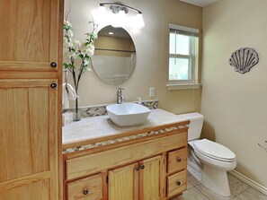 A bathroom with a wooden vanity, a white sink, a mirror, and a toilet. - Gulf Coast Getaway by Miss Kitty’s (Rockport)