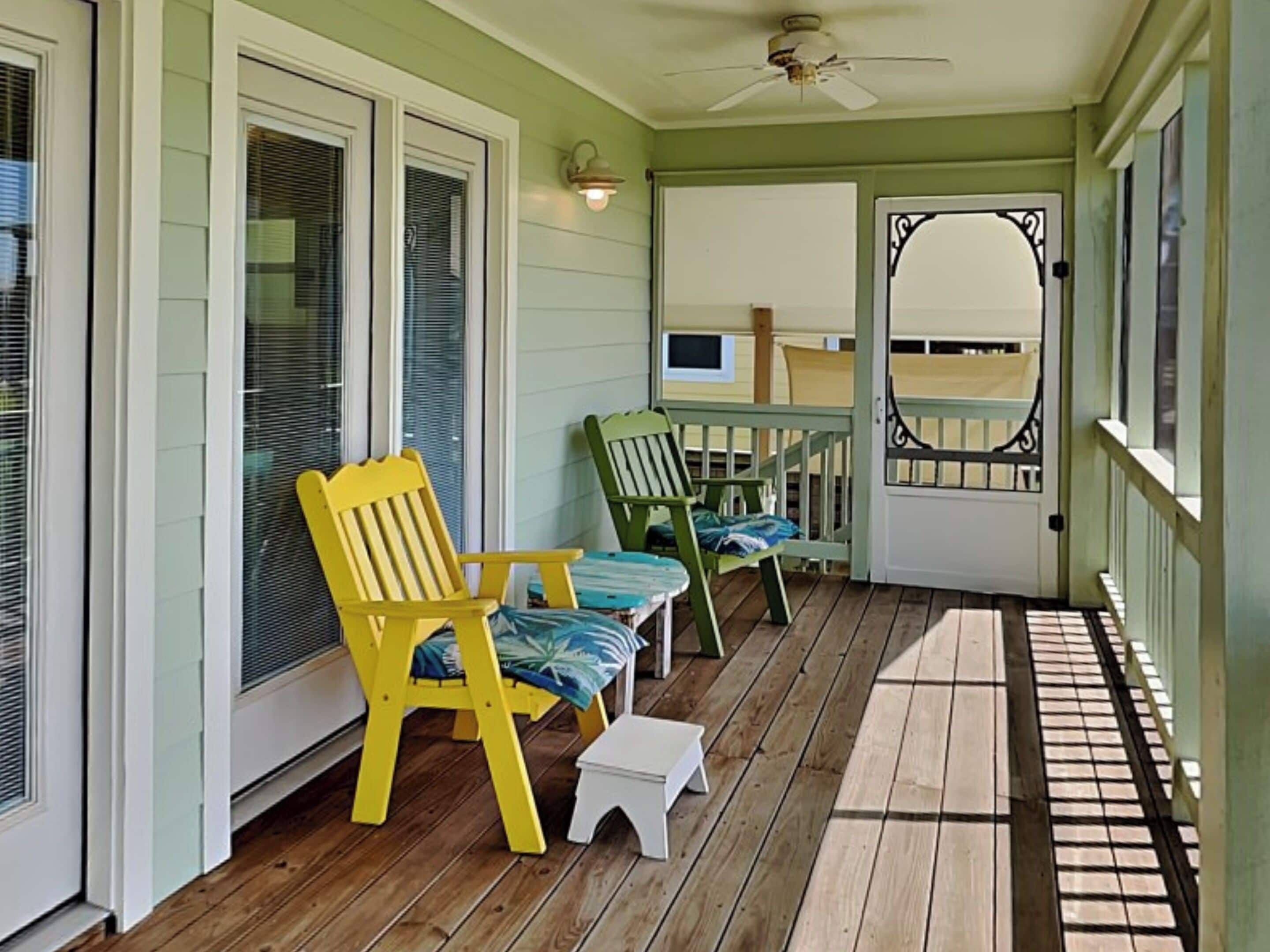 A porch with two Adirondack chairs, a small table, and a white step.
