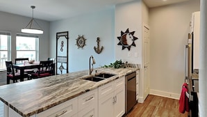 A kitchen with a marble countertop, white cabinets, and a wooden floor. - T's Getaway by Miss Kitty’s (Rockport)